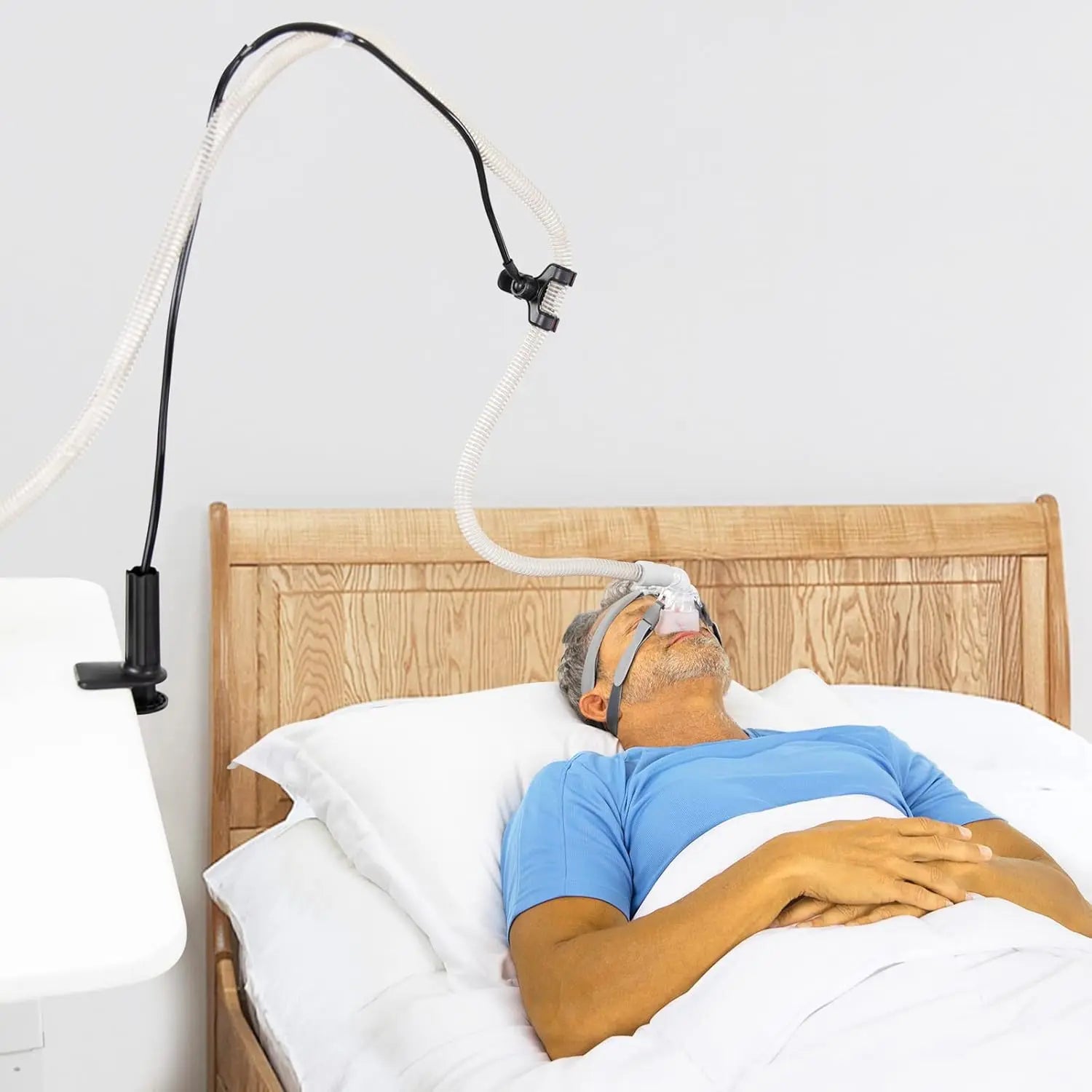 Man lying in bed with an oxygen mask and hose attached, on a white background
