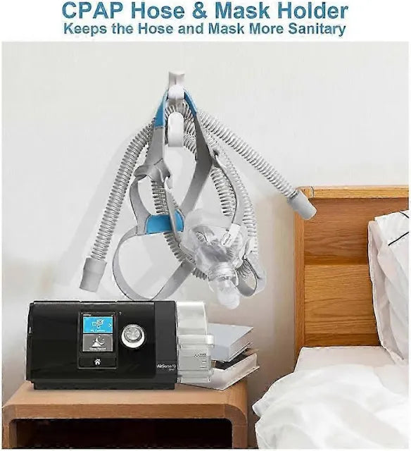 CPAP machine with hose and mask holder on a nightstand next to a bed.
