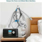 CPAP machine with hose and mask holder on a nightstand next to a bed.