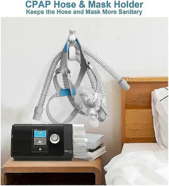 CPAP machine with hose and mask holder on a nightstand next to a bed.